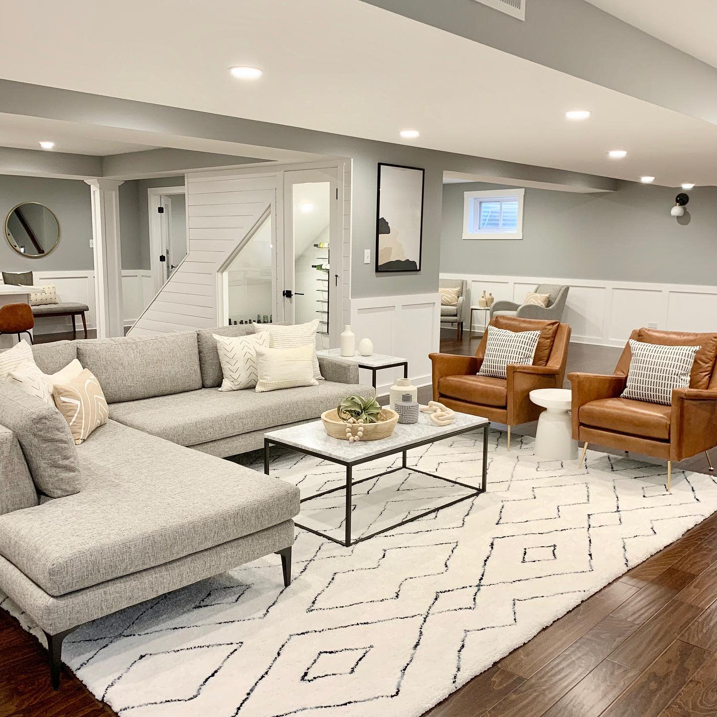 Modern basement living space with gray sectional, leather chairs, and patterned rug.